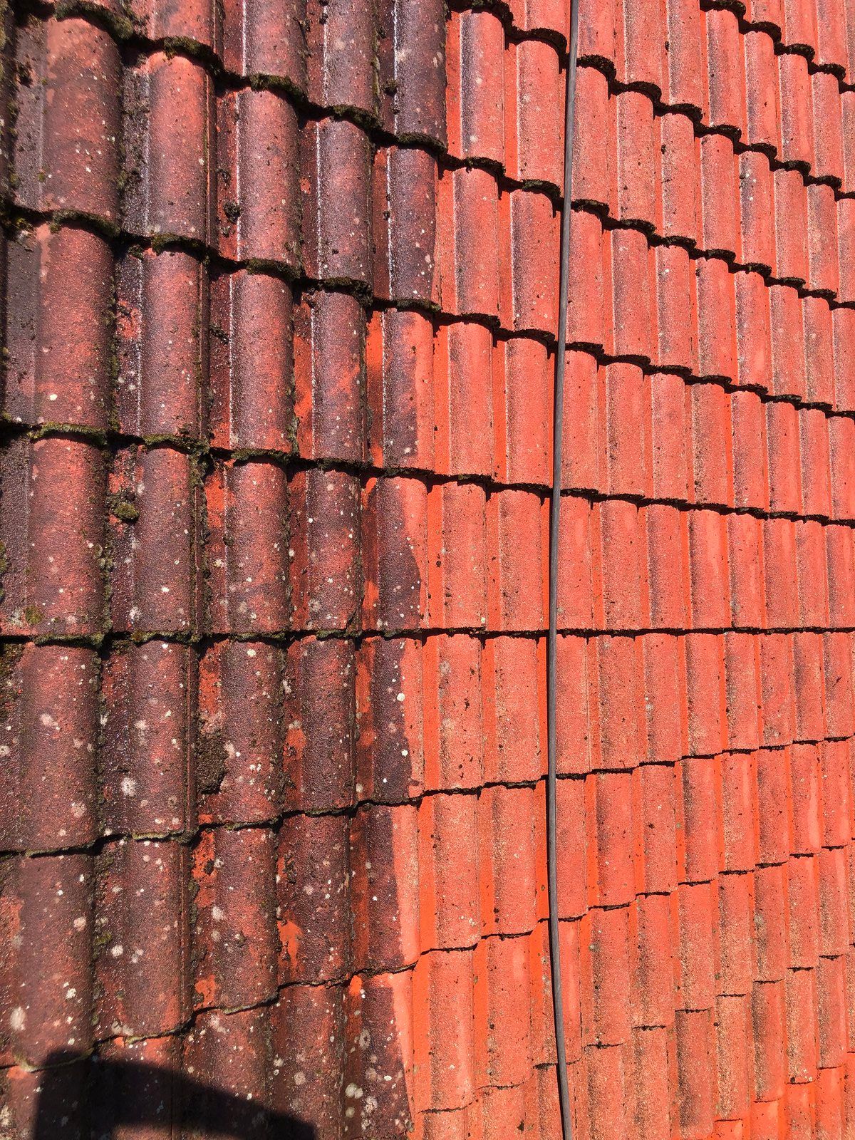 Mur de briques rouges avec un coin de bardeaux sombres et patinés, et du soleil sur le côté droit.