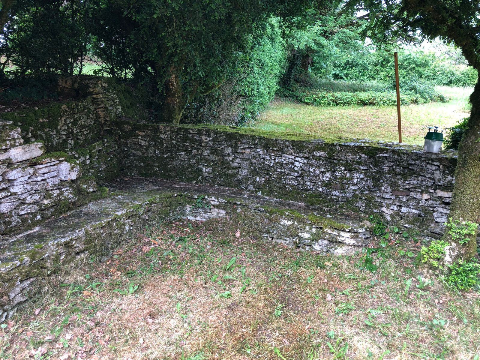 Coin de jardin clos de murs en pierre, avec sol moussu et arbres au-dessus