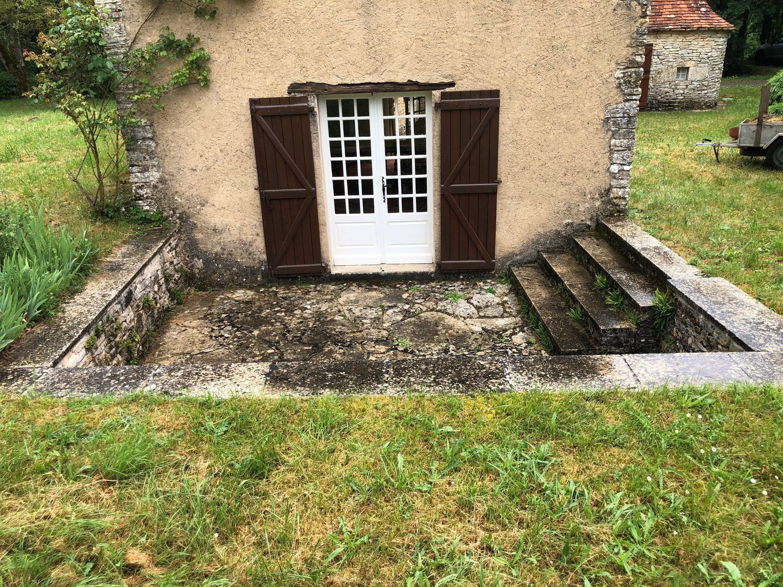 Petite porte de cottage avec volets bruns, marches en pierre et cour gazonnée devant