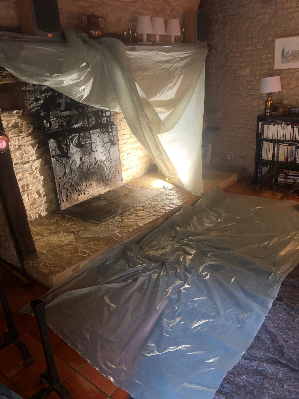 Salon dont les meubles sont recouverts de bâches en plastique, probablement pendant des travaux de rénovation ou de nettoyage.