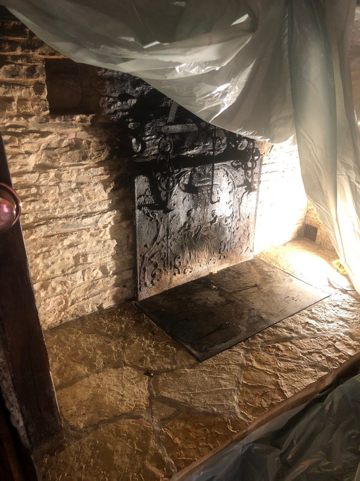 Cheminée en maçonnerie recouverte d'une bâche en plastique, avec un foyer en pierre humide et une lumière vive venant de la droite.