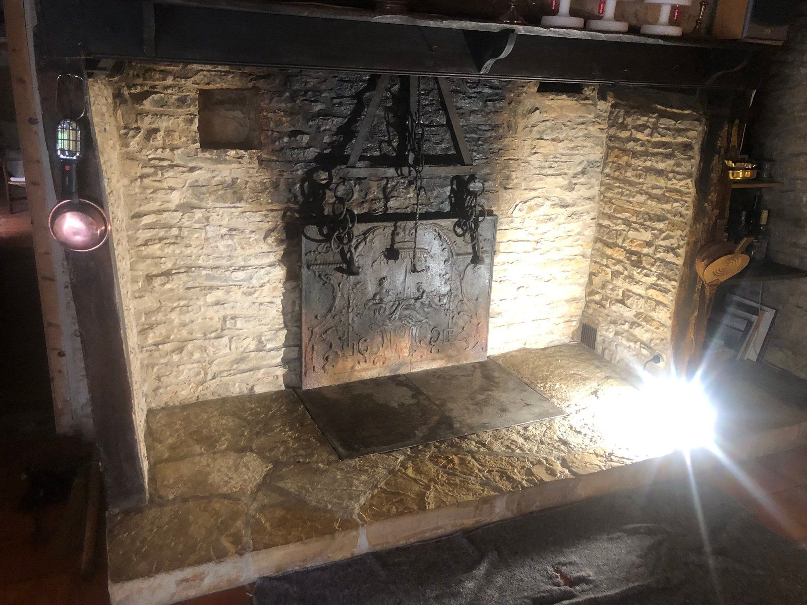 Cheminée en pierre avec une plaque de foyer en fer noir et un reflet vif en bas à droite