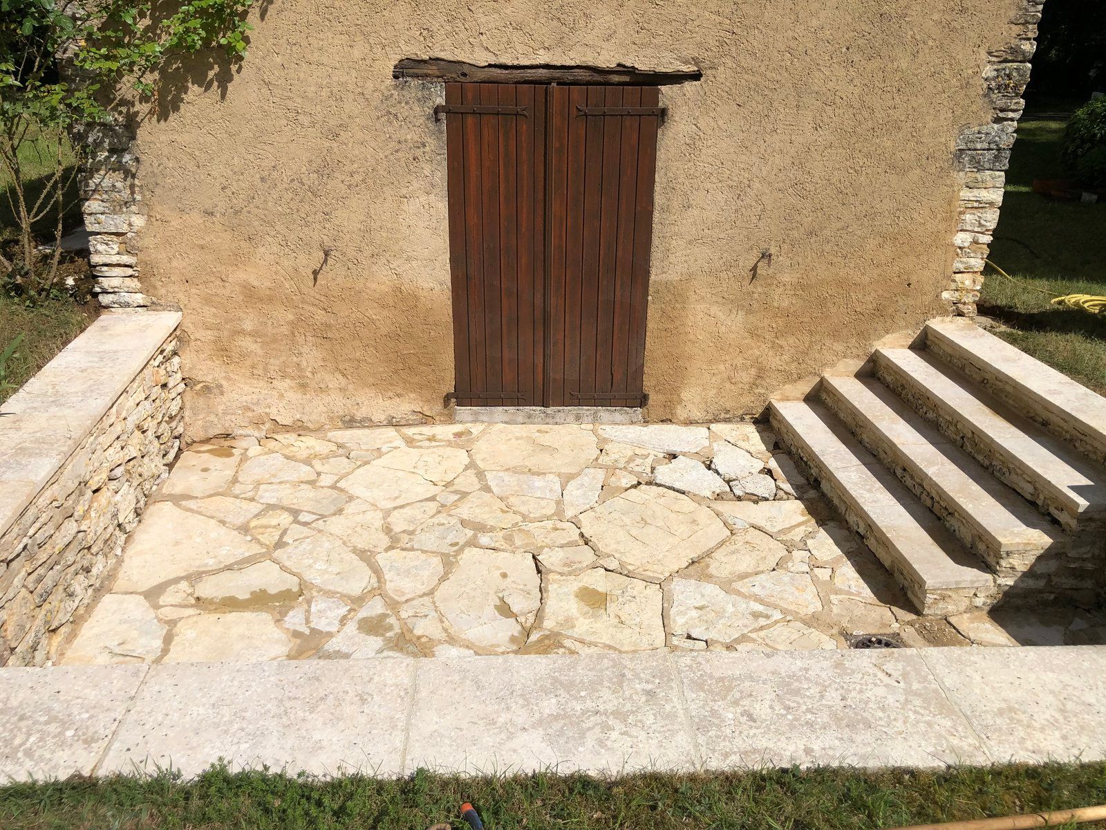 Cour en pierre avec une porte en bois dans un mur beige et des marches sur la droite