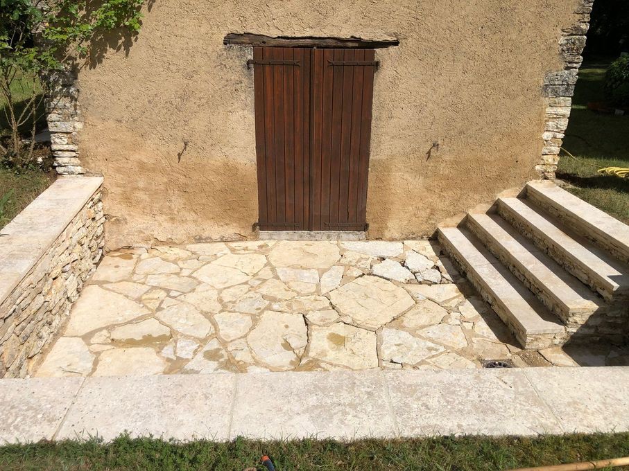 Cour en pierre avec une porte en bois dans un mur en stuc et des marches sur la droite