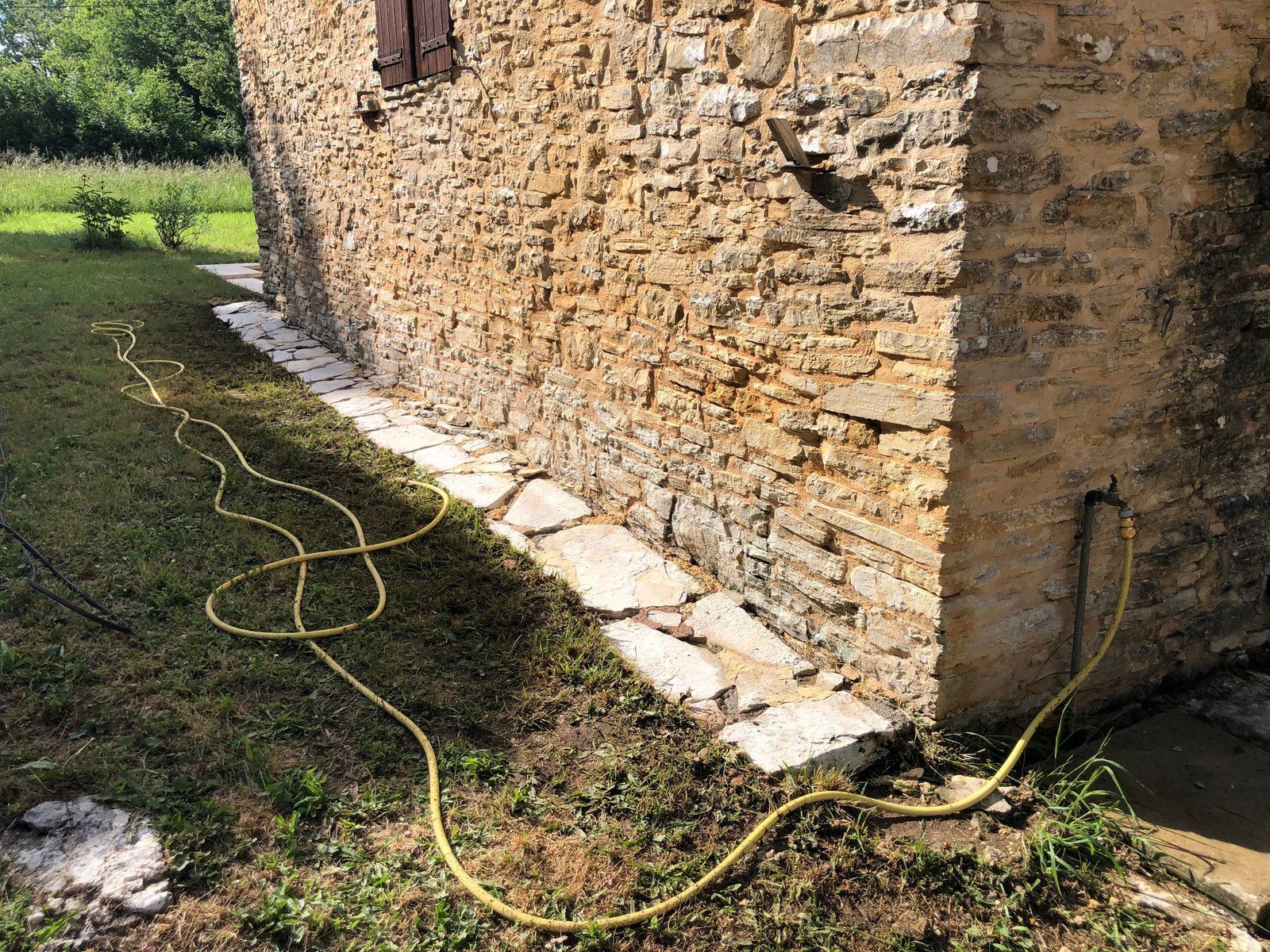 Tuyau jaune sur l'herbe à côté d'un bâtiment en pierre au soleil