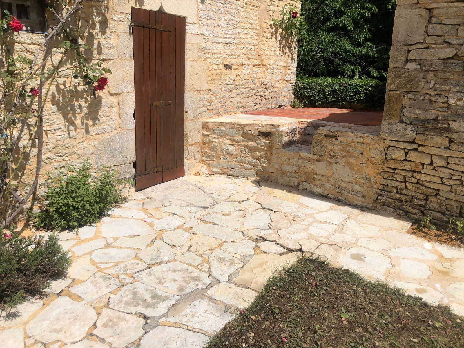 Cour en pierre avec une porte en bois, un muret et des dalles ensoleillées.