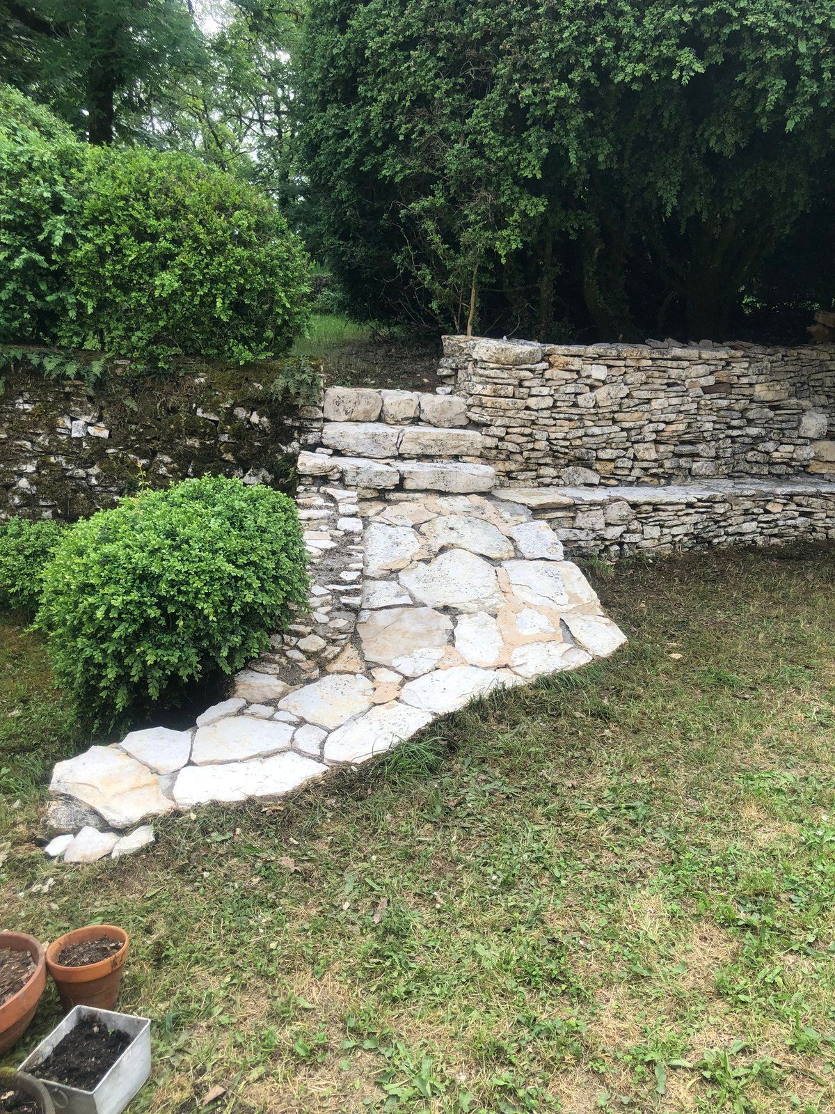 Escaliers en pierre d'une terrasse dans un jardin avec arbustes et gazon, partiellement recouverts de matériau de réparation blanc