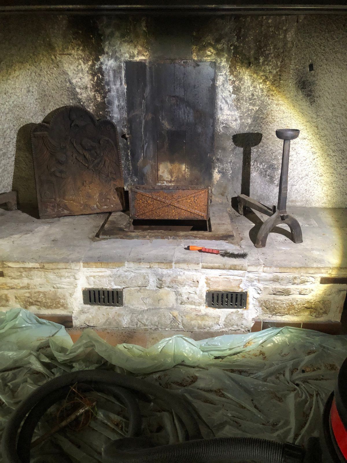 Cheminée en pierre avec grille métallique, conduit de cheminée noirci par la suie et outils de cheminée sur le foyer.