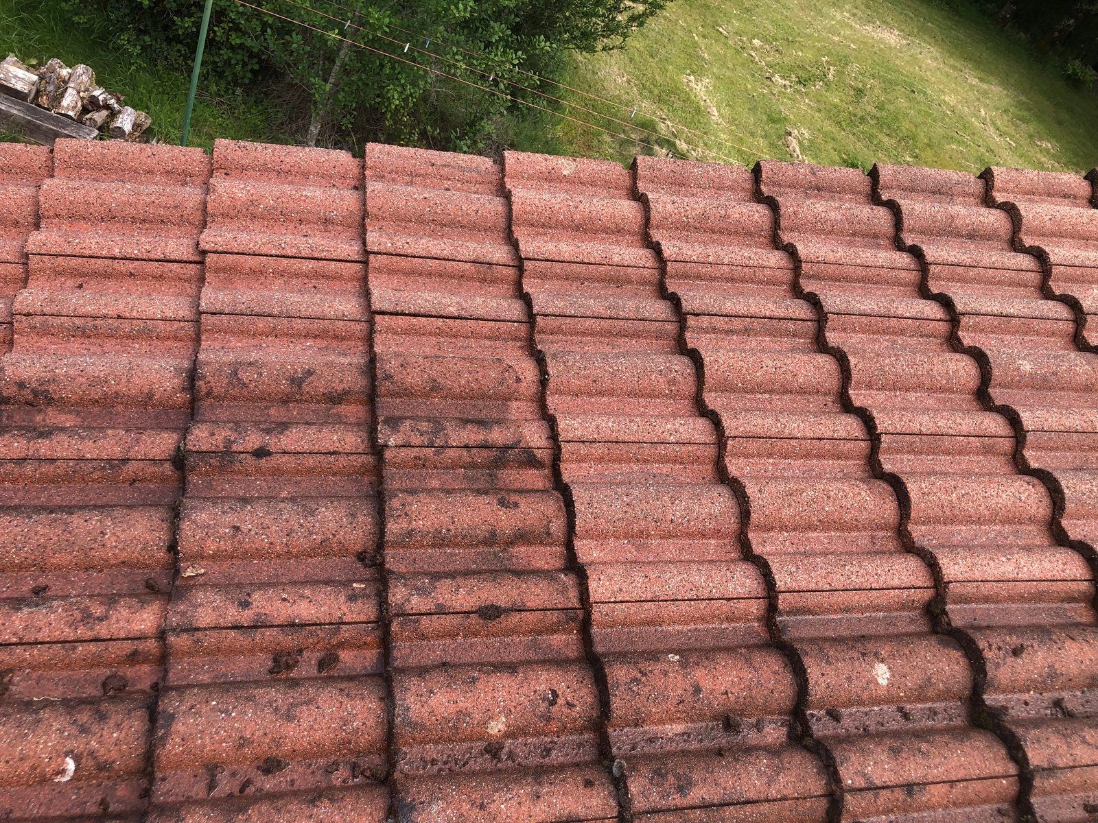 Des tuiles rougeâtres empilées en rangées ondulées, vues du dessus sur un coin d'herbe verte.