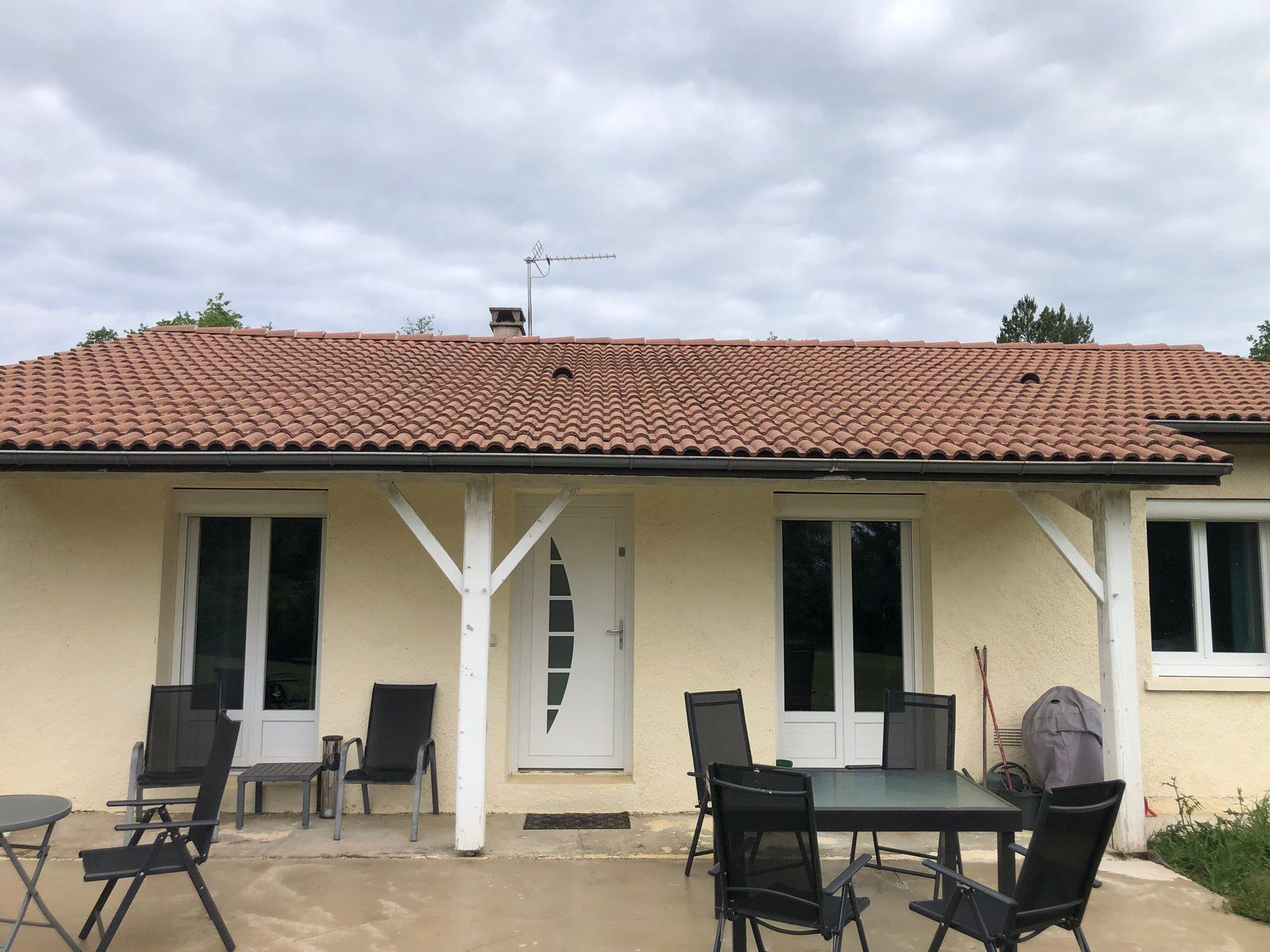 Terrasse avec table et chaises de jardin devant une maison couleur crème au toit de tuiles rouges.