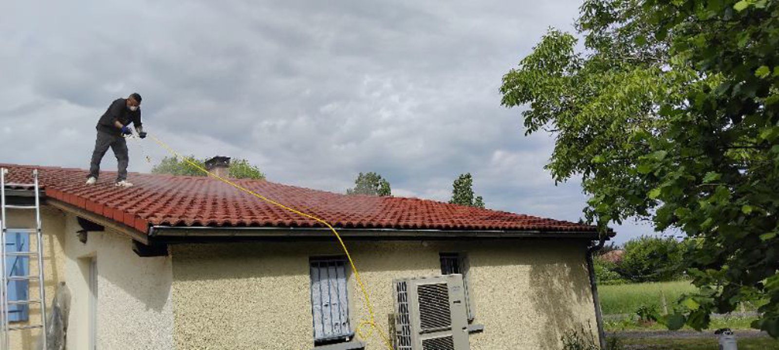Ouvrier réparant une maison sur un toit de tuiles rouges sous un ciel nuageux