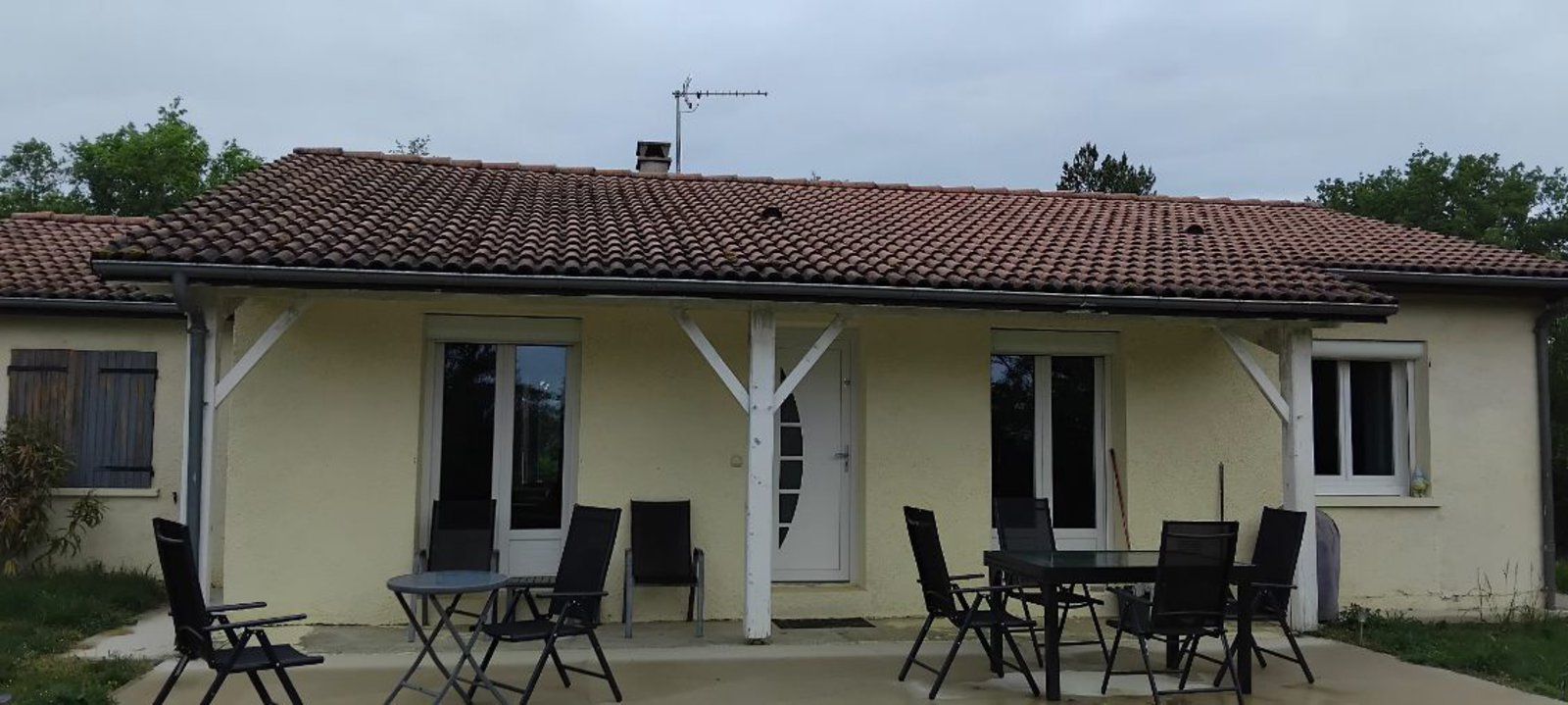 Maison de plain-pied couleur crème avec toit de tuiles et chaises de patio dans la cour avant