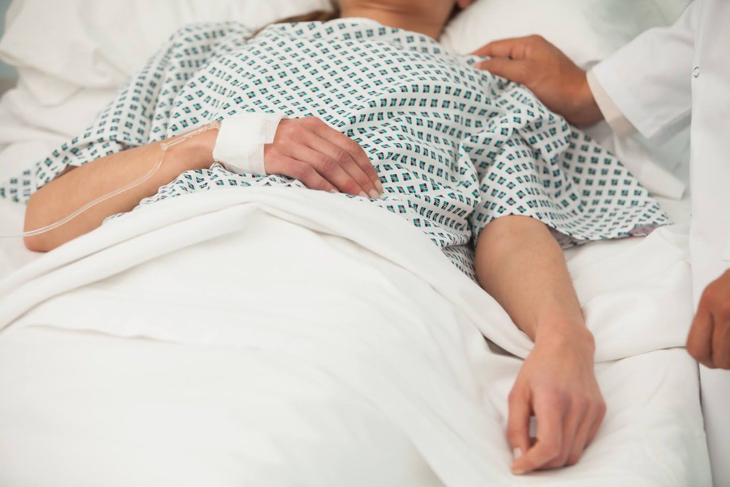 Person in hospital bed with IV and a doctor's hand on their shoulder.