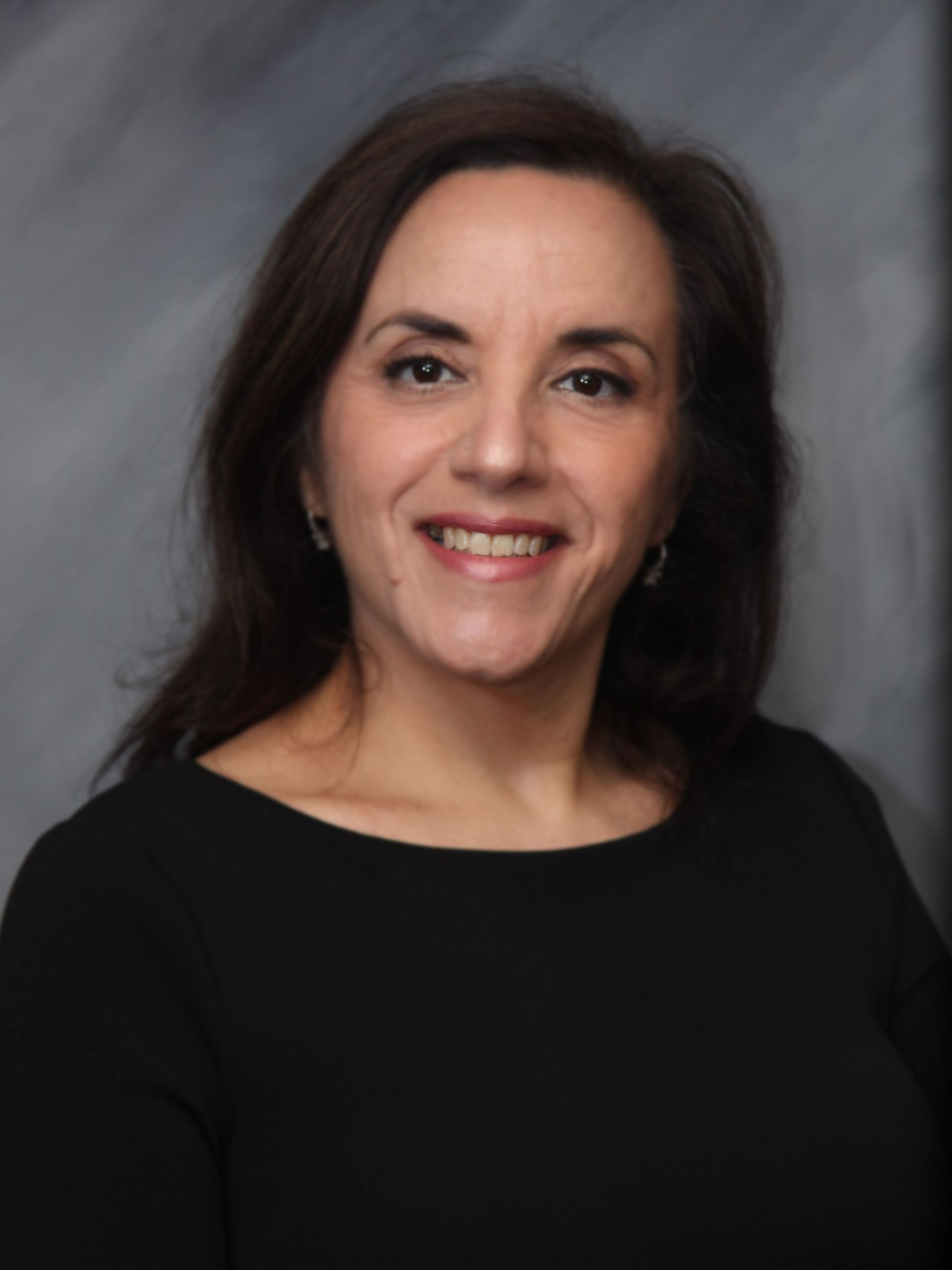 Woman with dark hair smiles, wearing a black top against a grey background.