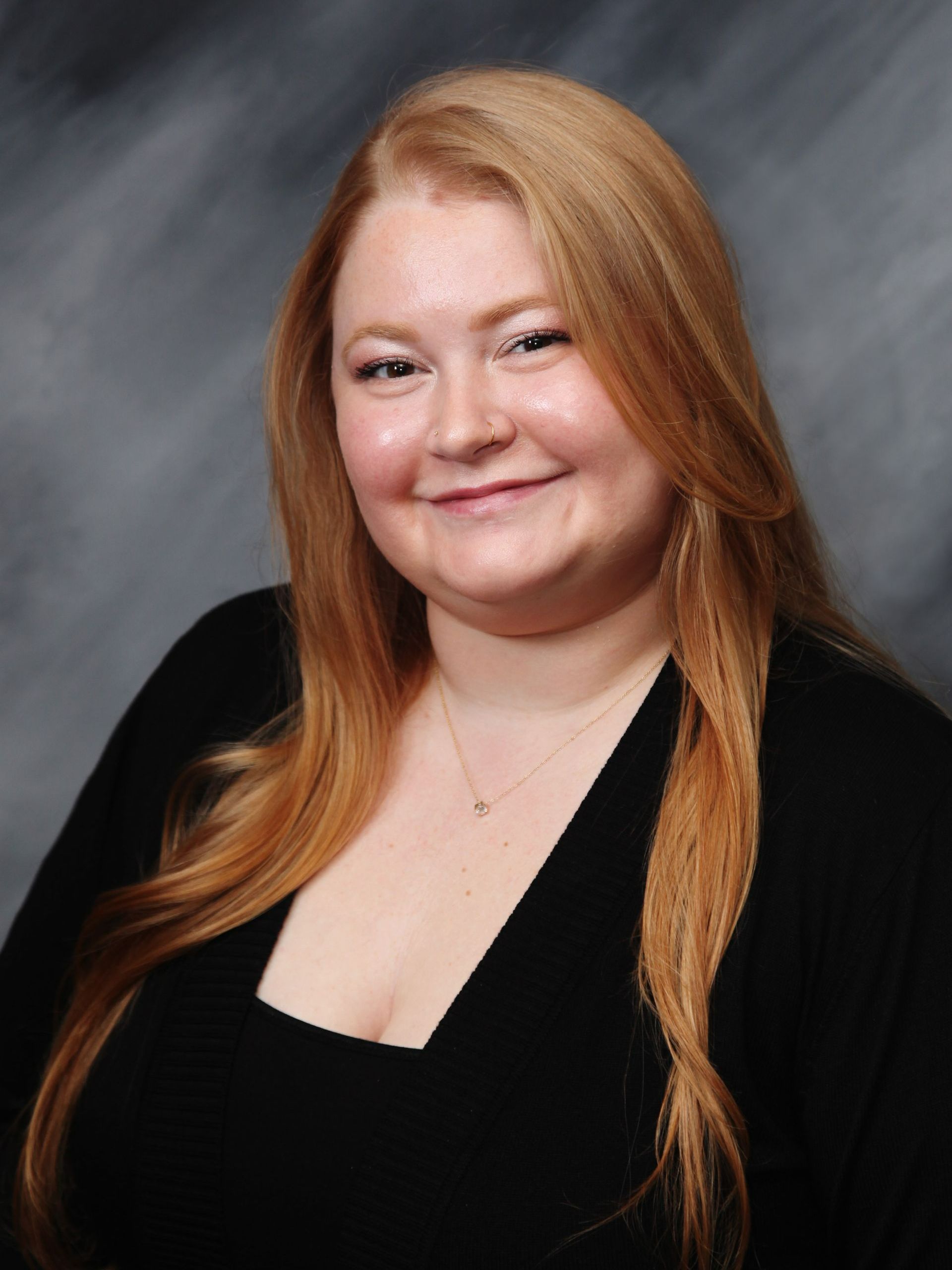 Woman with long red hair, smiling, wearing a black top against a blurred background.
