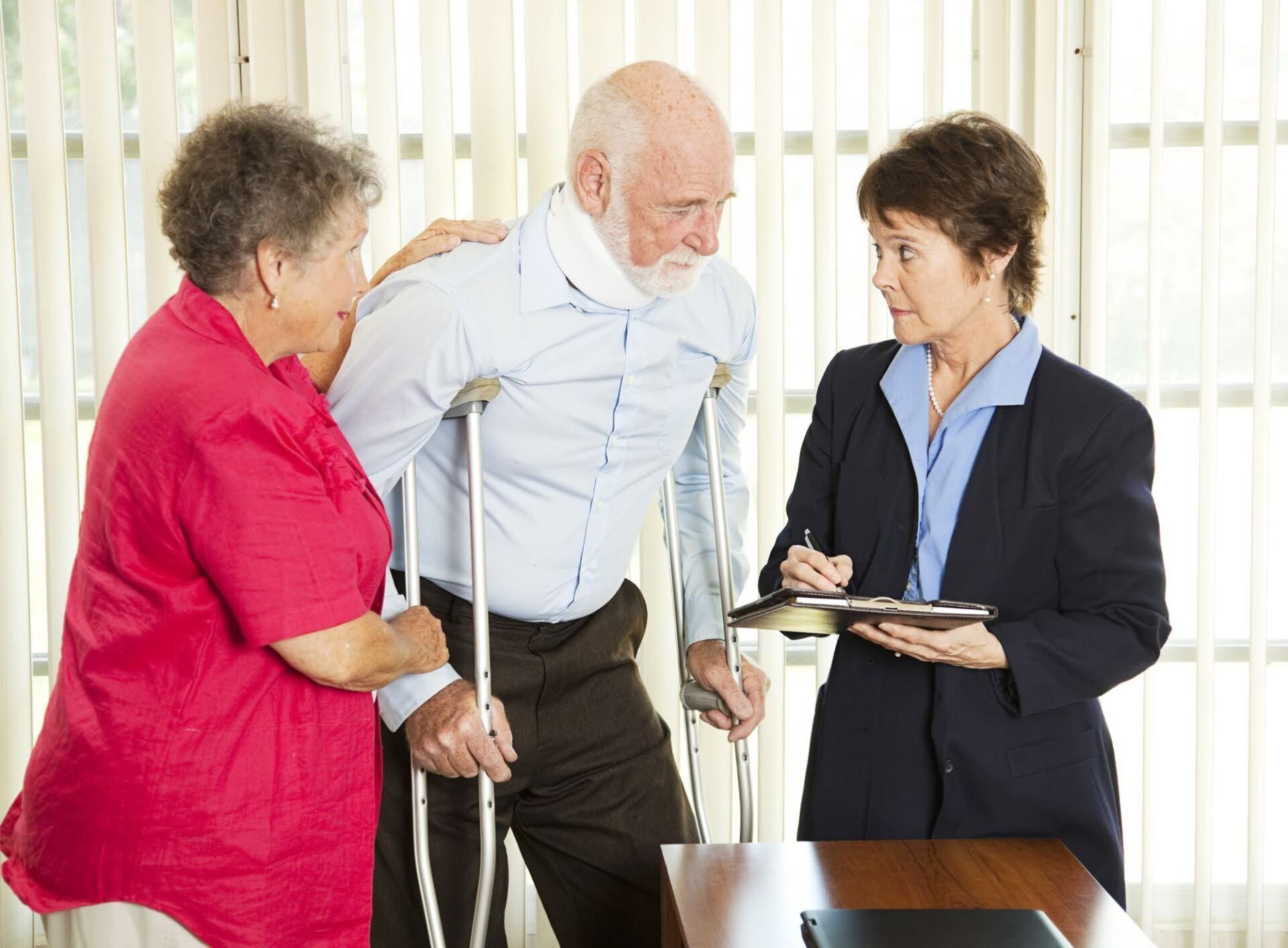 Man with neck brace and crutches, and woman assisted by another woman. They are talking to a person holding a notepad and pen.