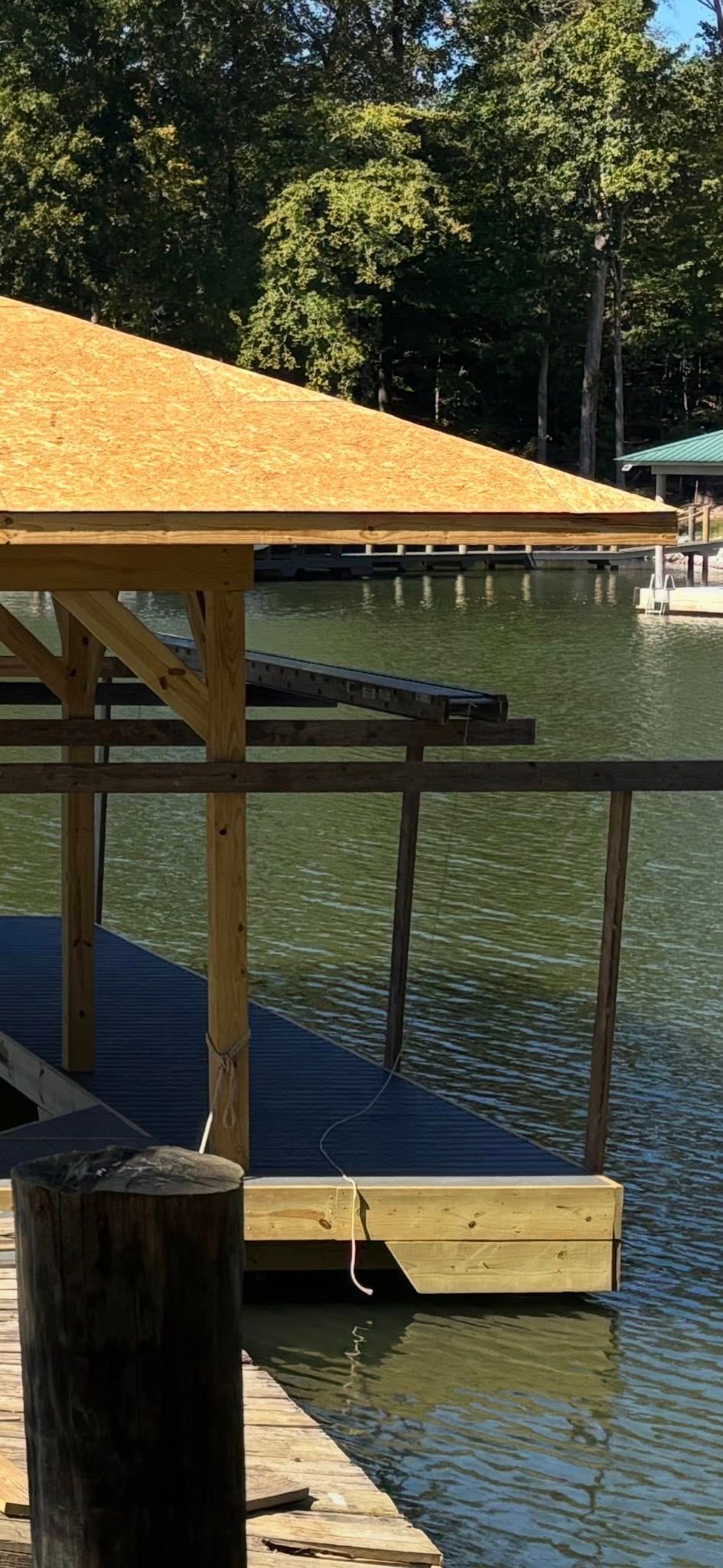 A wooden boat dock with a freshly shingled roof over the slip, situated on a calm lake with trees in the background.