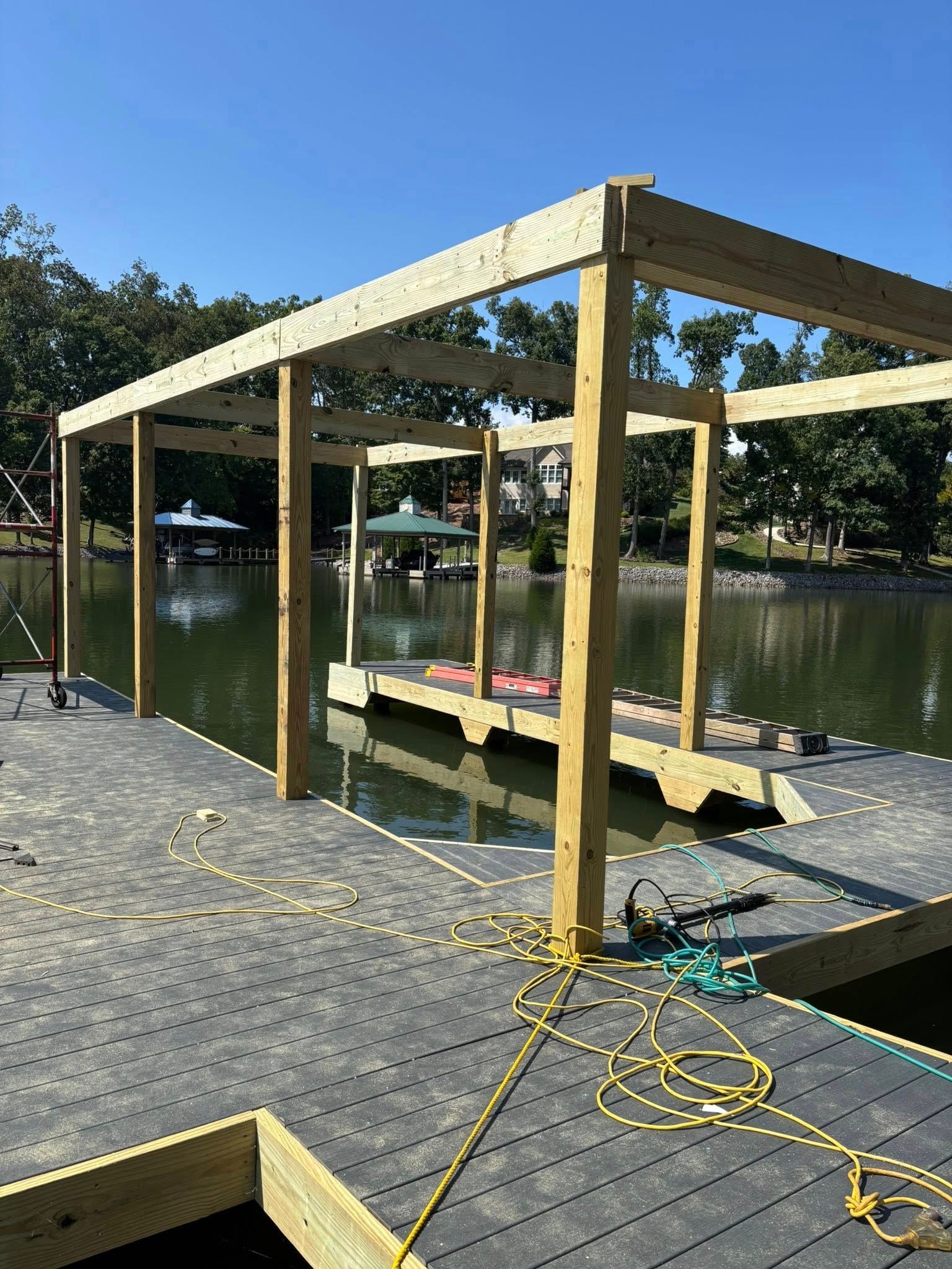 A wooden frame structure being built on a grey floating dock over a calm lake.