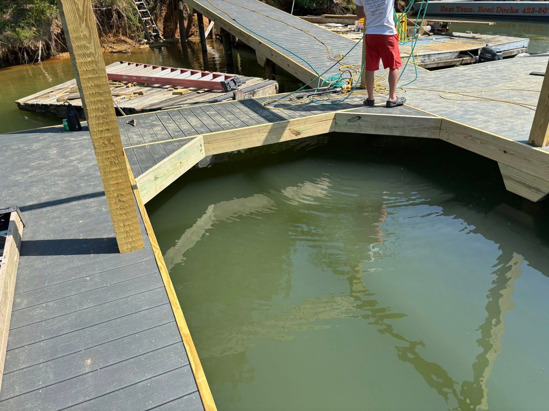 A person stands on a wooden deck overlooking murky water, next to a slanted ramp leading to a floating dock.