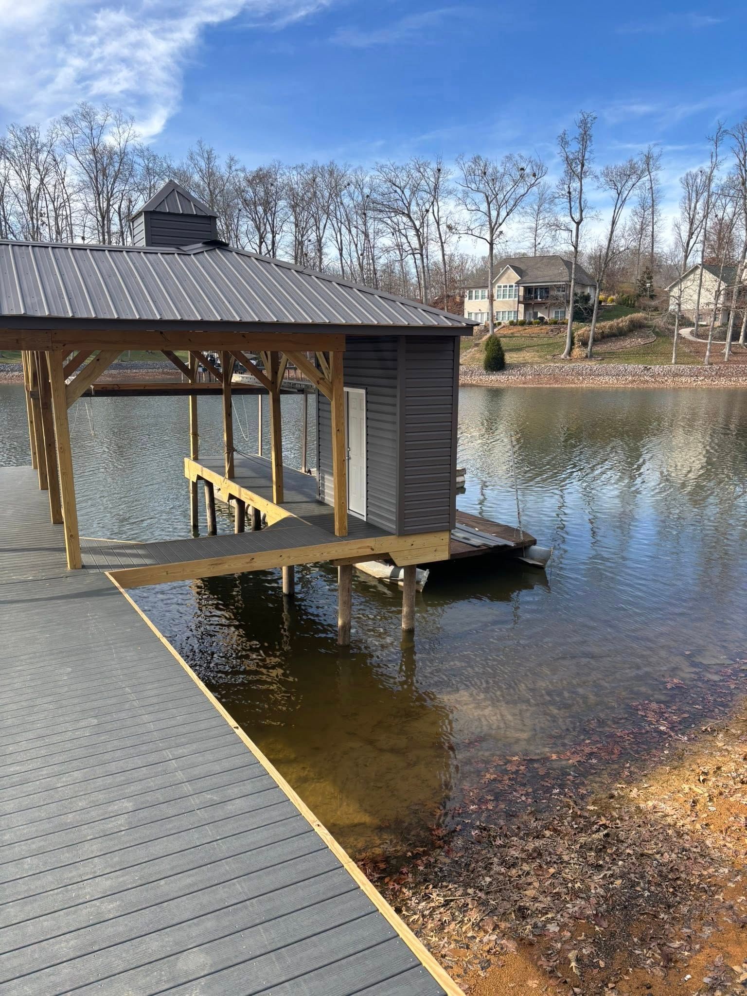 A wooden boat dock with a covered storage shed extends over a calm lake, with residential houses visible on the shore.