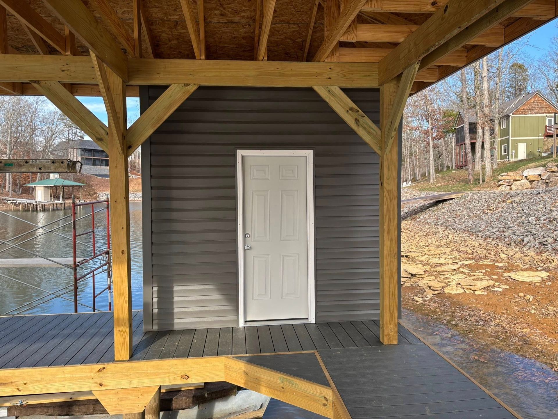 A gray storage shed with a white door sits on a wooden dock overlooking a lake.