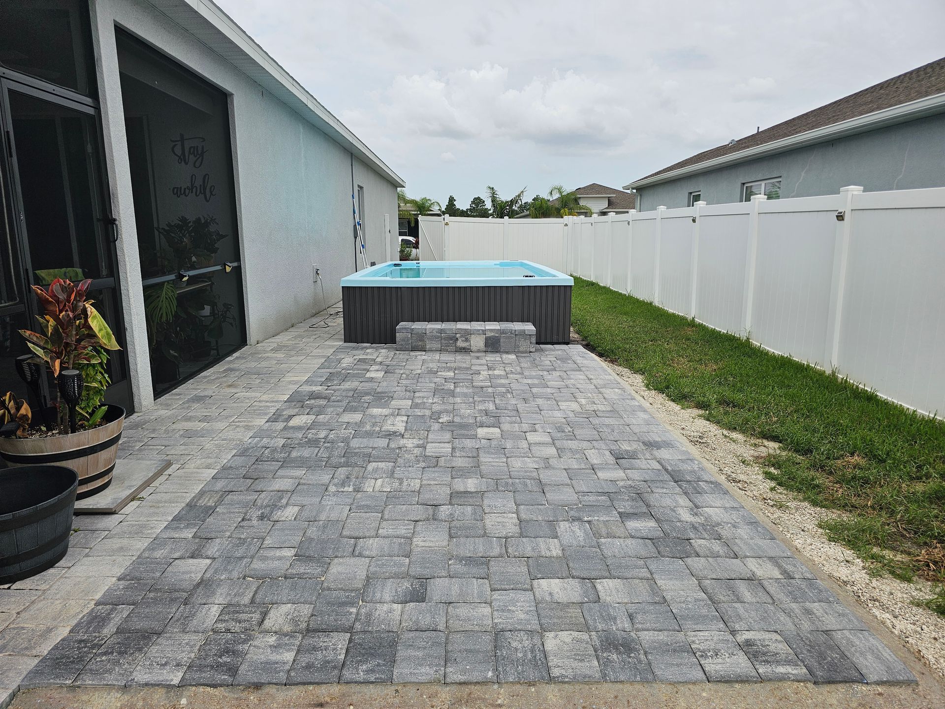 Backyard with a paved patio, hot tub, white fence, and a house.
