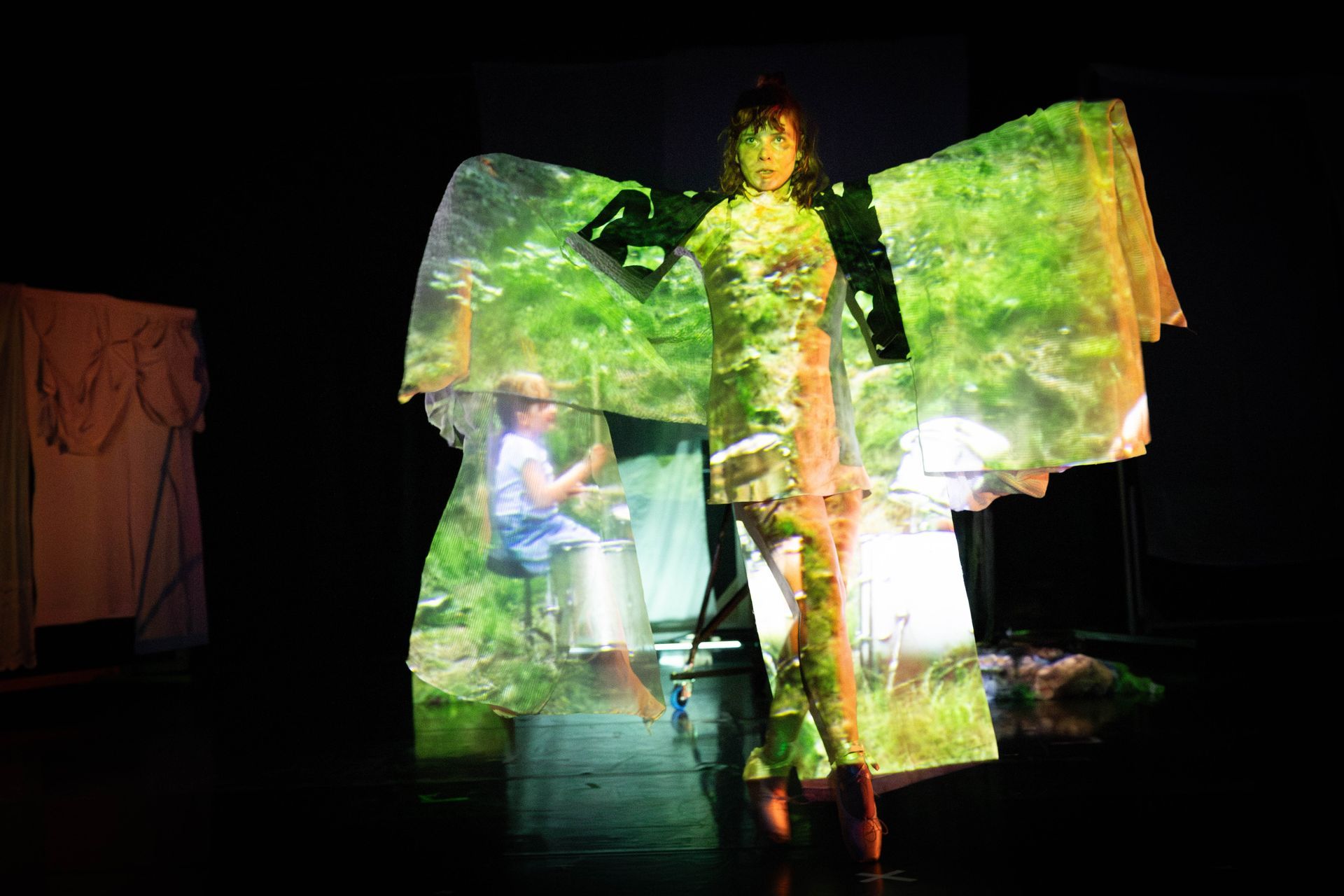 Vrouw met geprojecteerd natuurbeeld, trommel en achtergrond, verlicht podium.