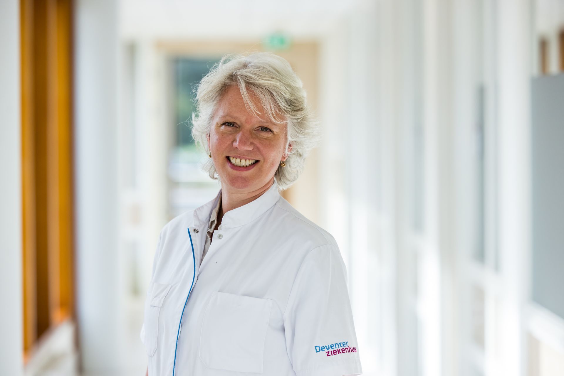 Lachende vrouw in een witte laboratoriumjas in een ziekenhuisgang.