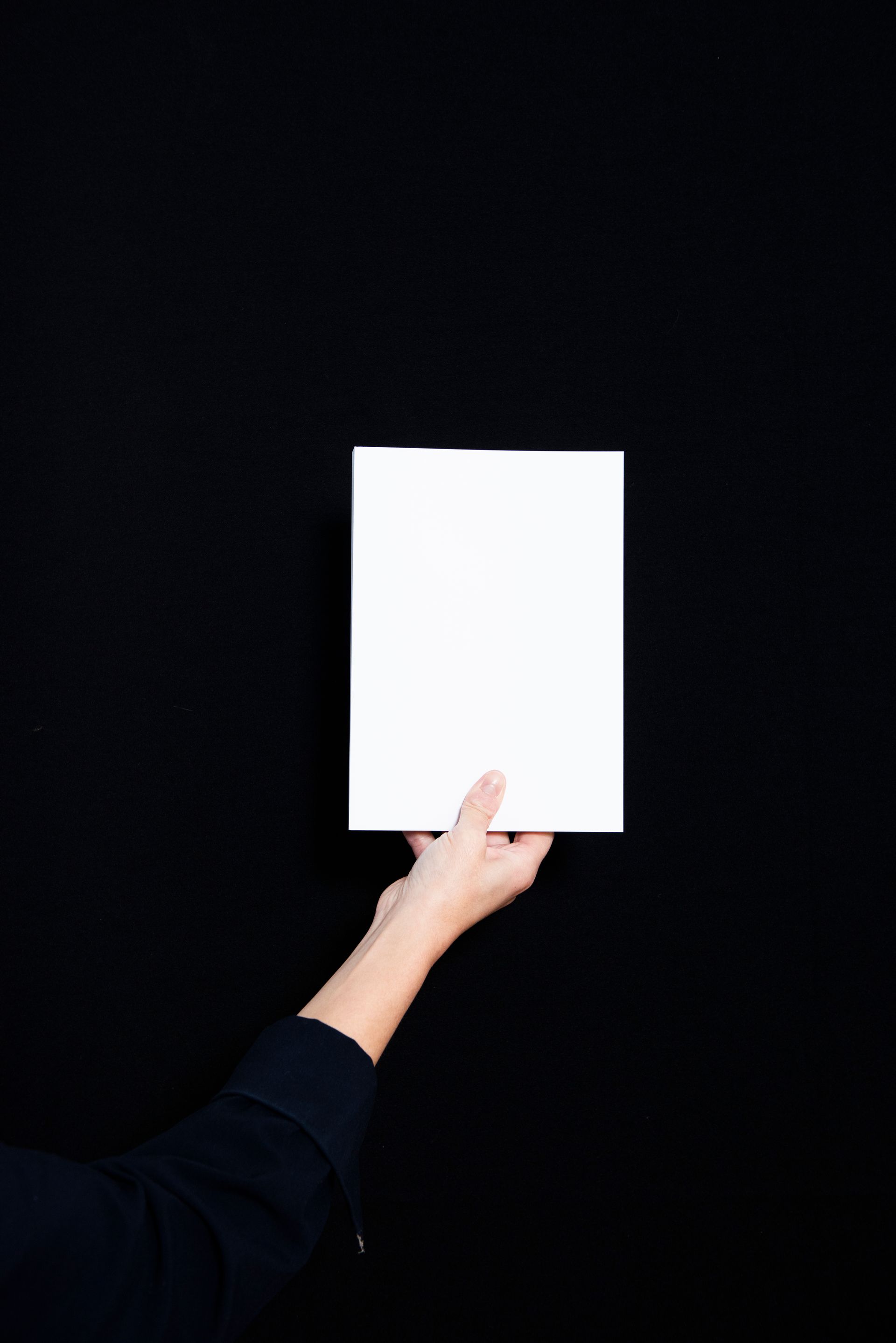 Hand die een wit, blanco vel papier vasthoudt tegen een zwarte achtergrond.