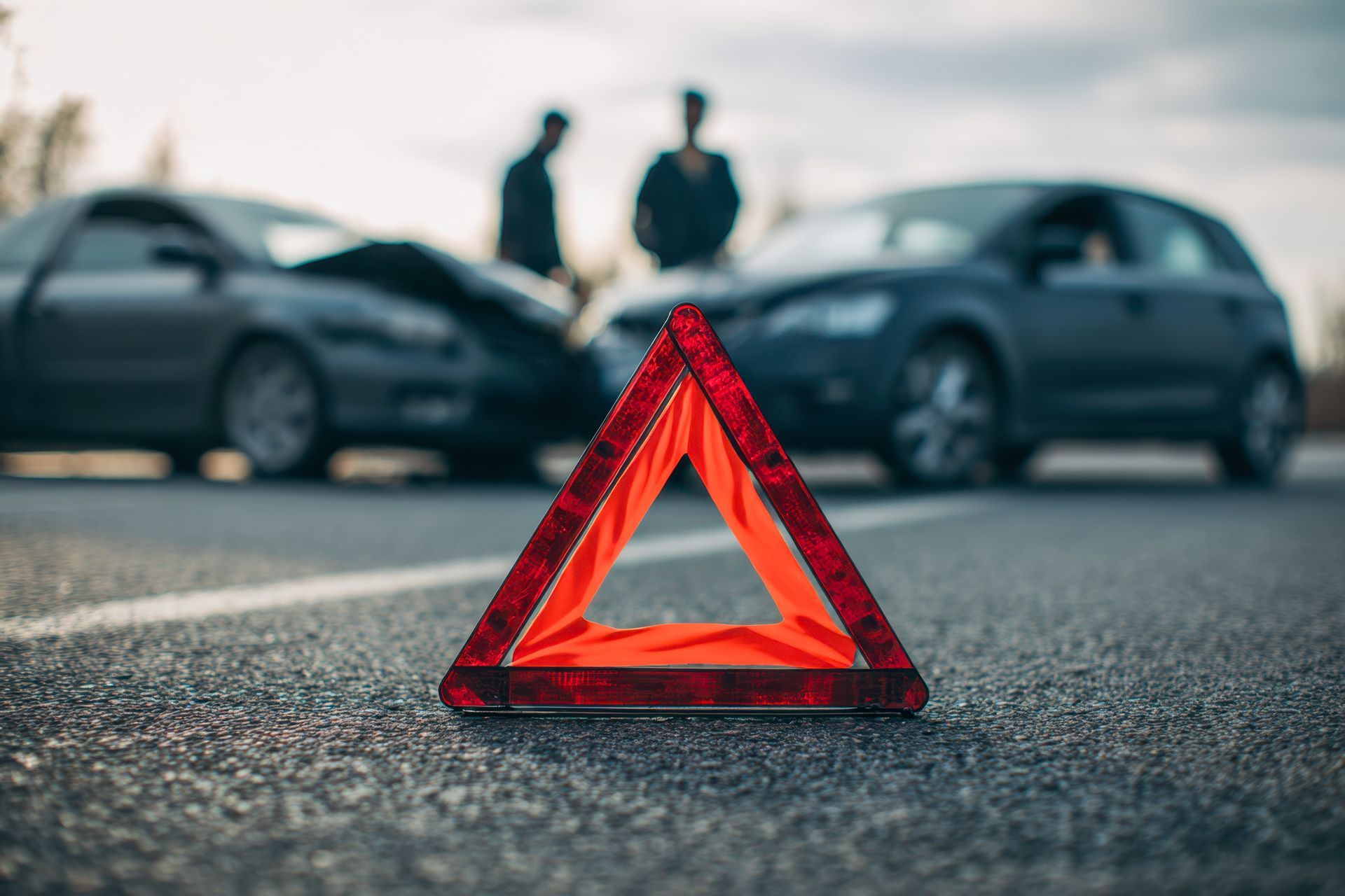 Reflective warning triangle on road with two damaged cars and people discussing the accident