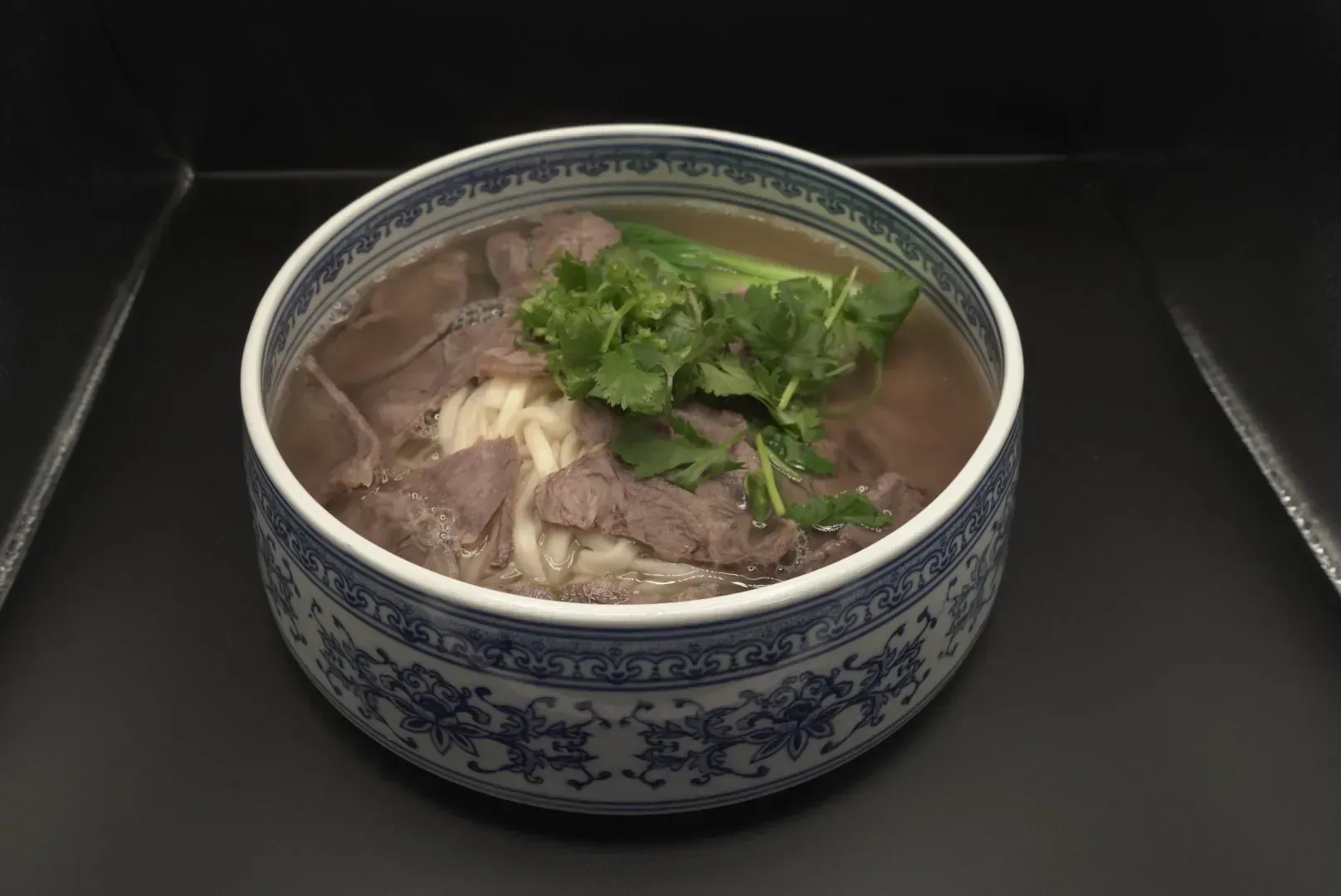 Blue-and-white bowl of noodle soup topped with beef and cilantro