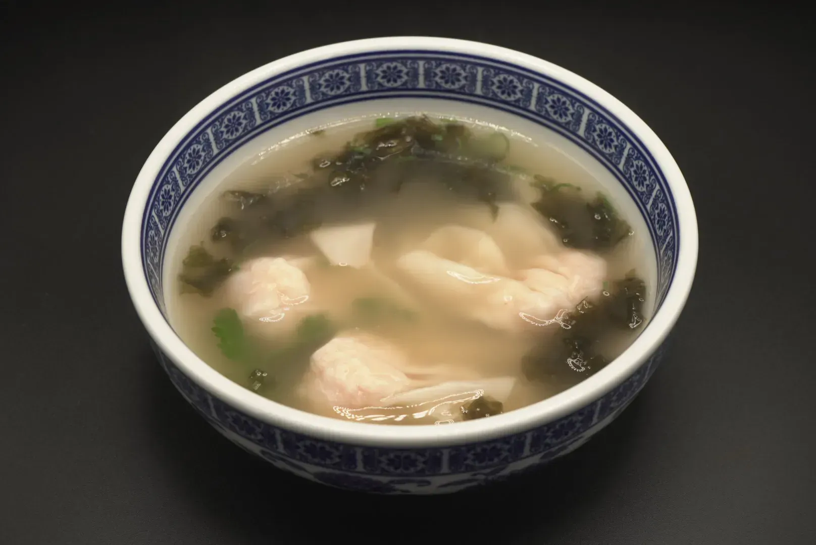Bowl of clear soup with dumplings and greens in a blue-and-white patterned bowl