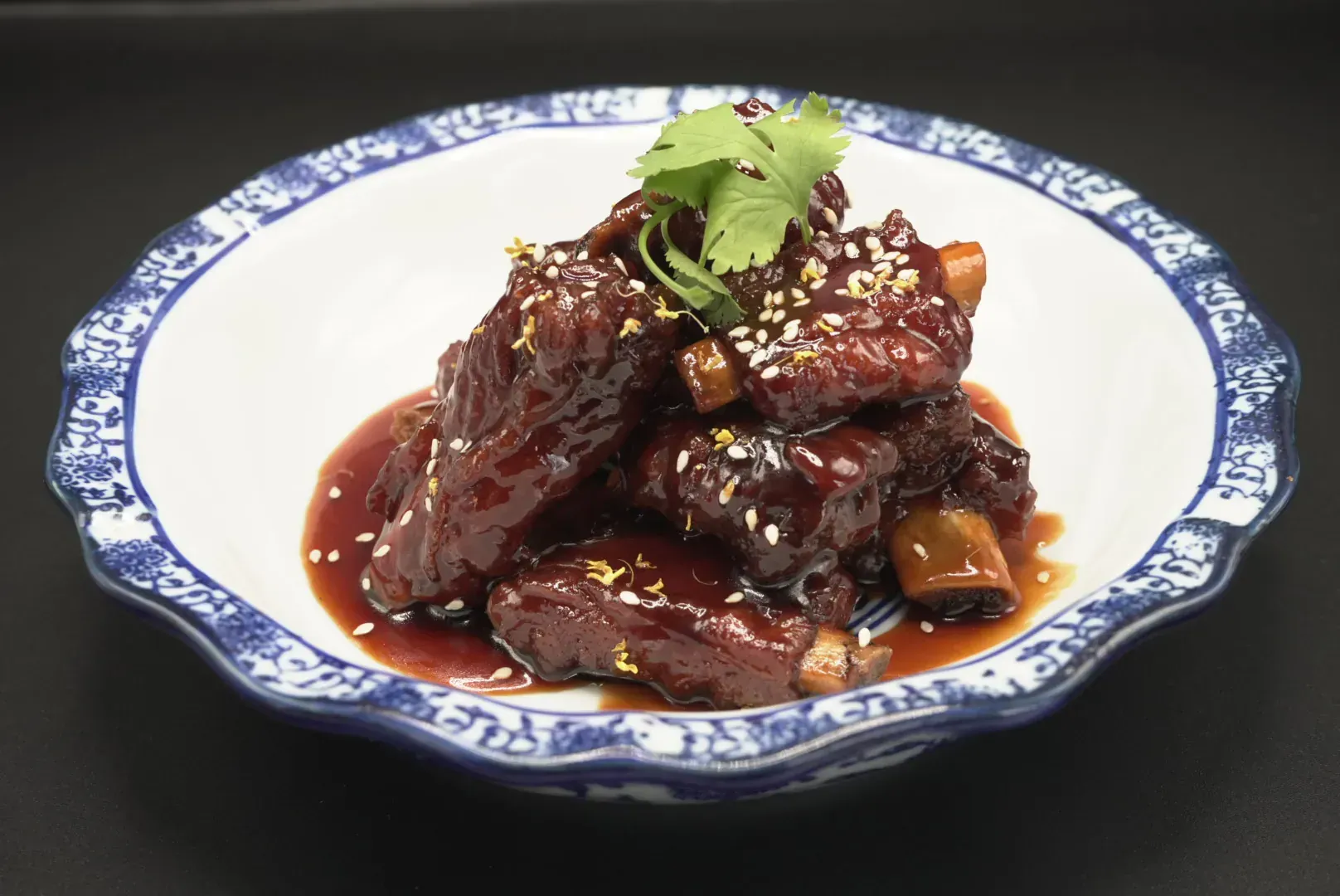 Braised meat in dark sauce on a blue-and-white plate, garnished with cilantro and sesame seeds.