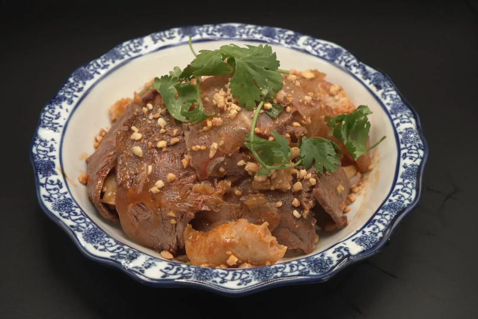 Braised meat dish topped with peanuts and cilantro in a blue-and-white bowl