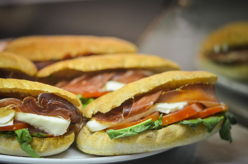 Panini con prosciutto, mozzarella, pomodoro e lattuga, su un piatto bianco.