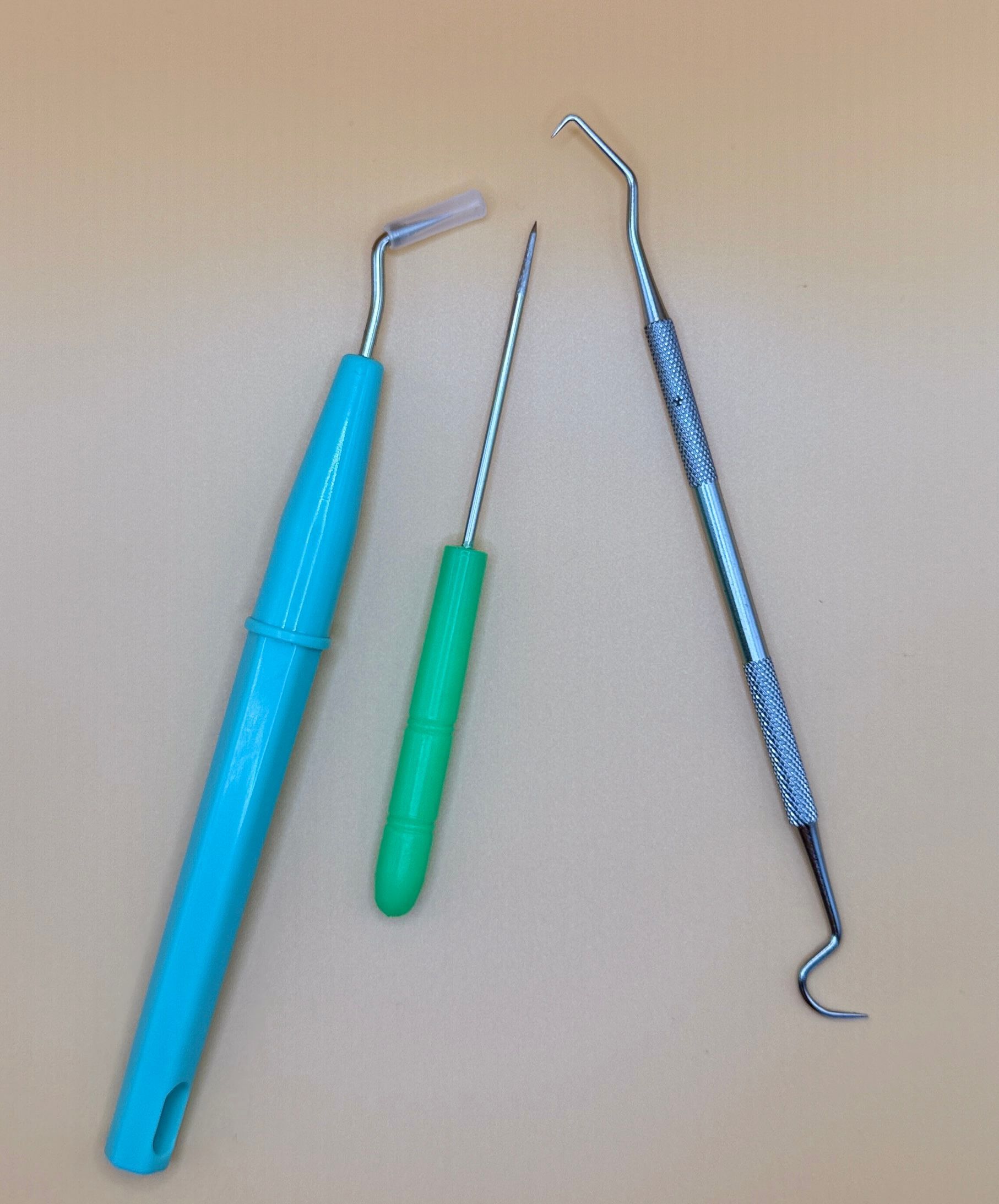 Three dental tools with curved metal tips and colored handles on a beige surface.