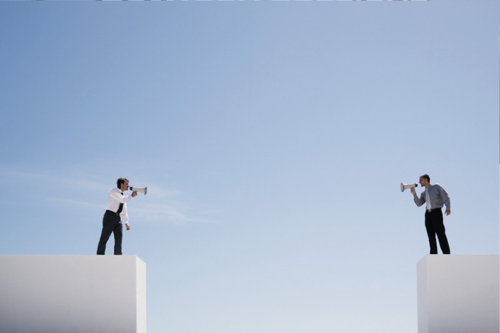 Two people standing on separate platforms using megaphones to communicate across a gap, representing