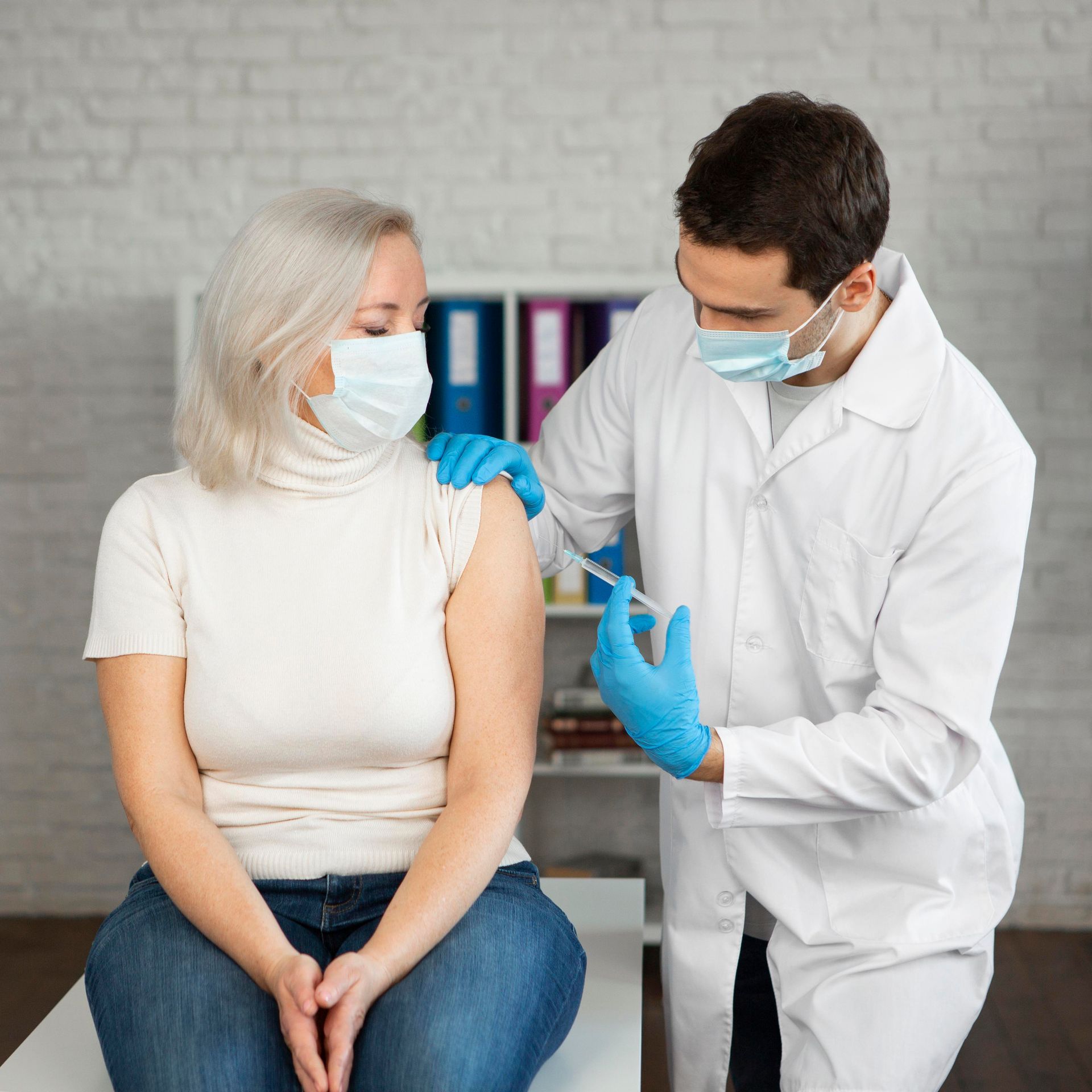 A woman wearing a mask is getting a vaccine from a doctor.