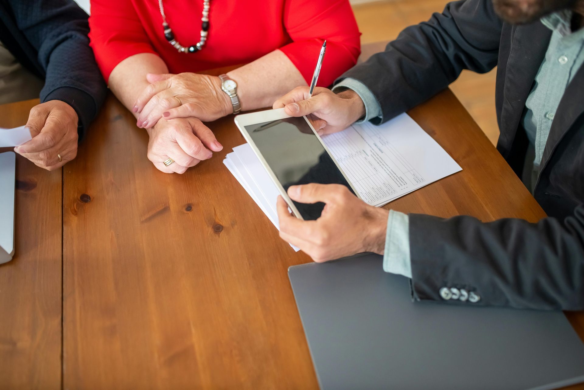 People in business attire reviewing documents and using a tablet at a wooden conference table