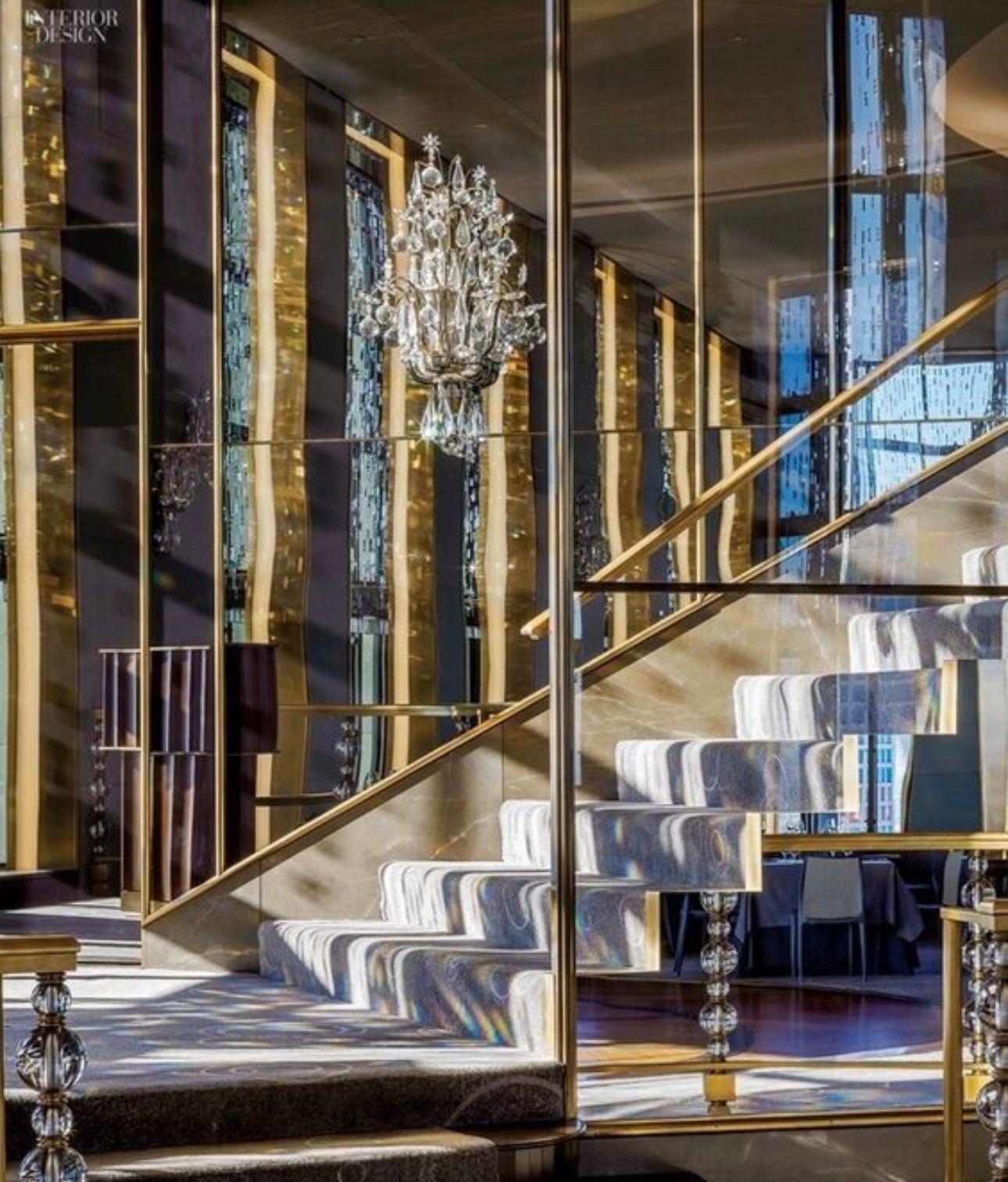 Luxurious staircase with gold accents, crystal chandelier, and sunlight streaming through windows.