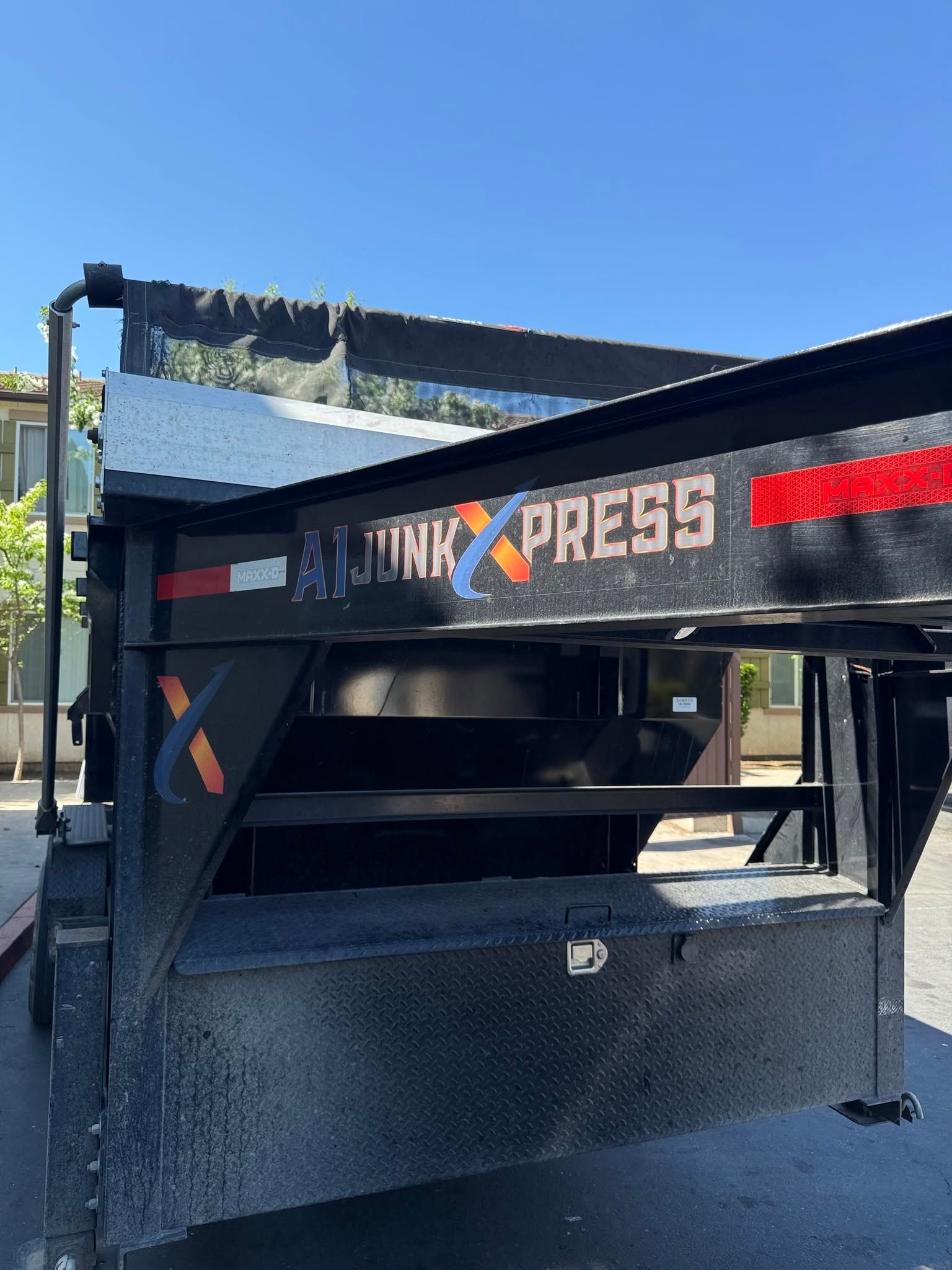 Black JUNK XPRESS dumpster with red logo, outdoors under a blue sky.