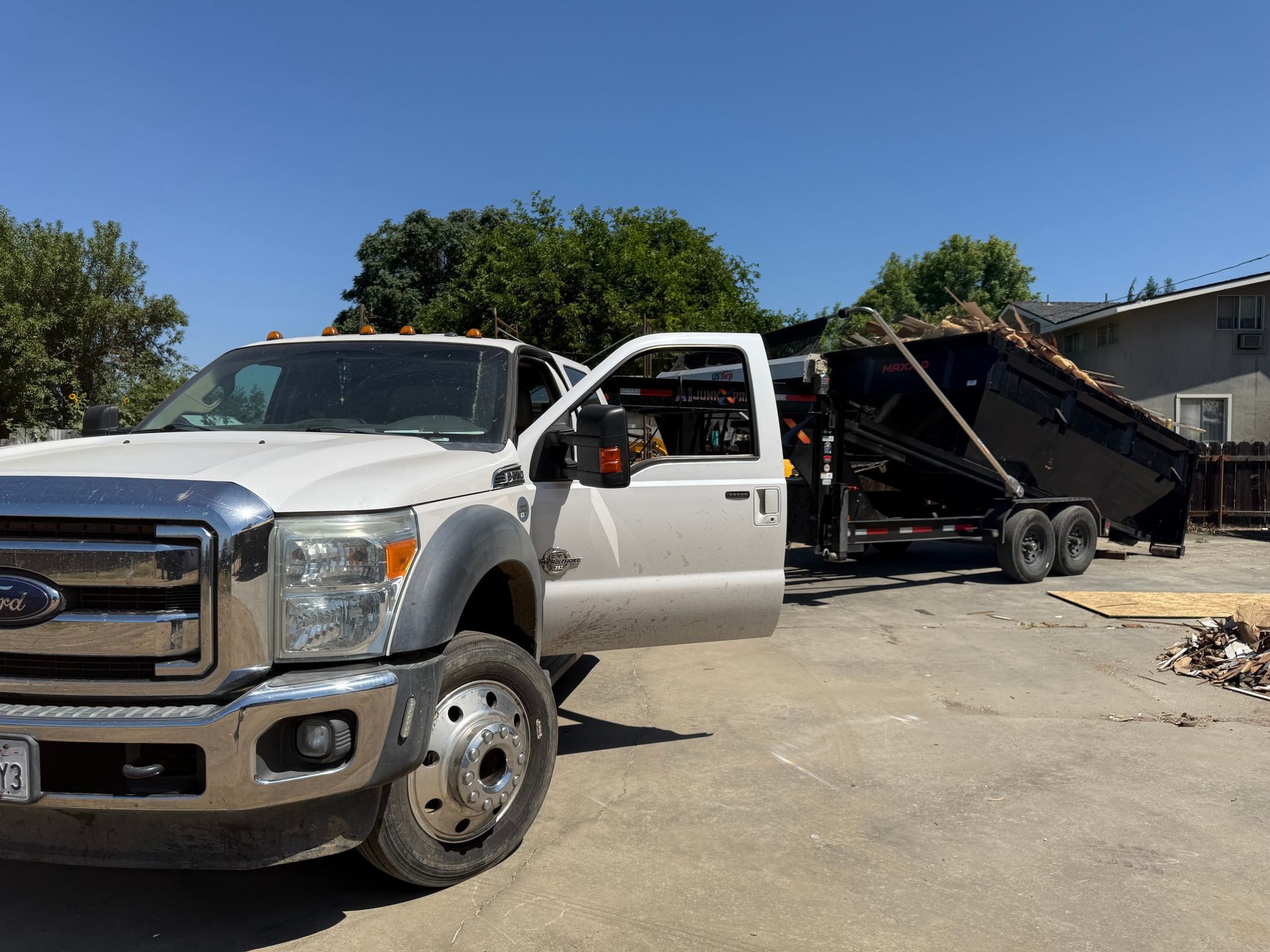 Worker kneeling beside a large metal dumpster being loaded onto a flatbed truck in a driveway