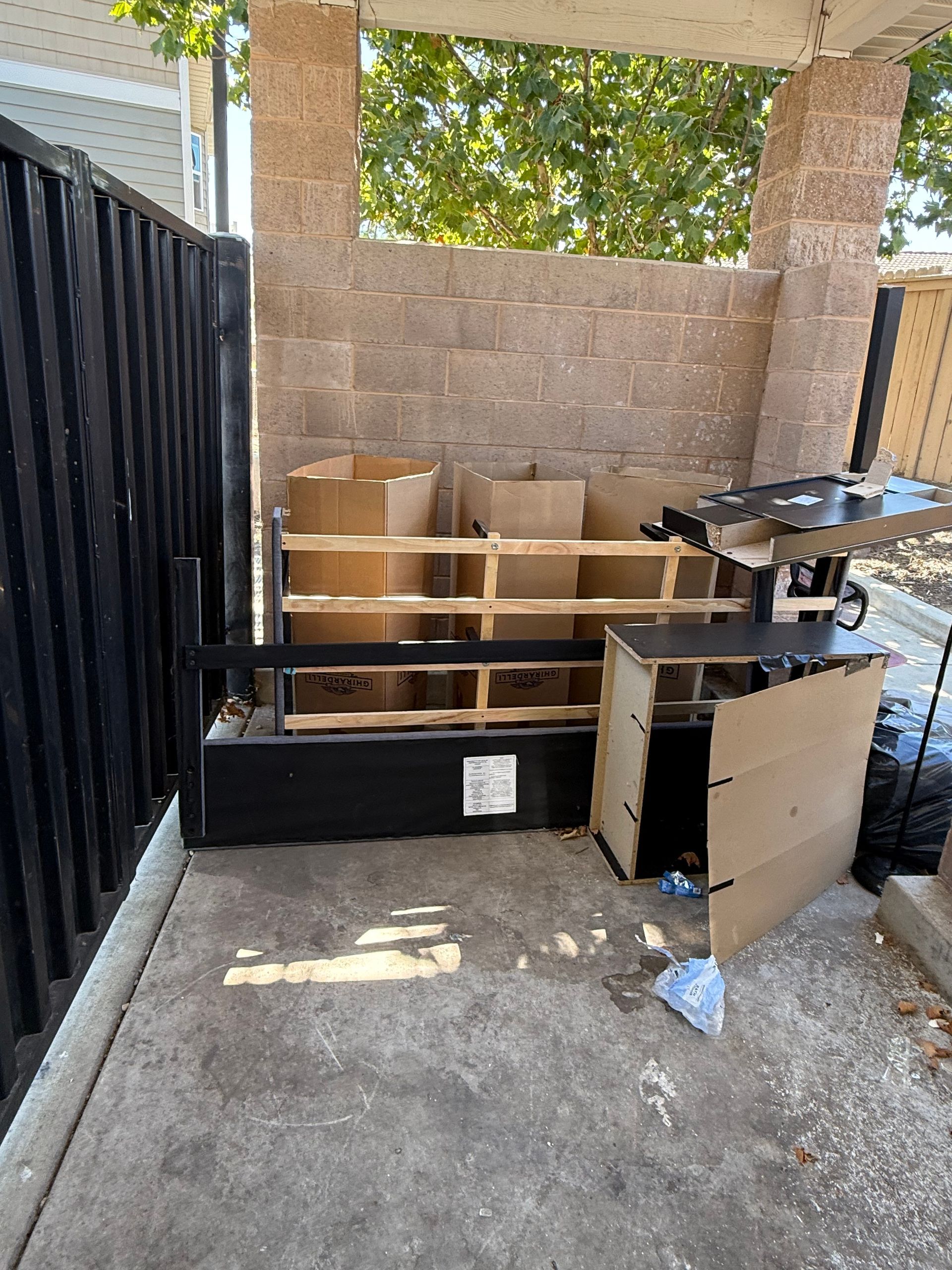 Garage packed with boxes and household items, with a person moving items beside a driveway in bright sunlight