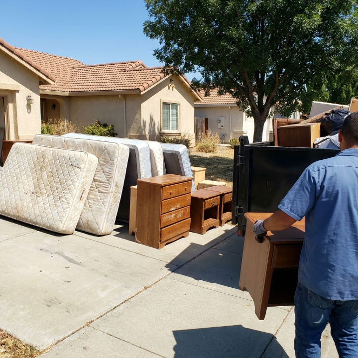 Man moving a dresser and mattresses on a driveway outside a suburban house