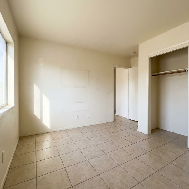 Empty beige bedroom with tiled floor, window light, and open closet area