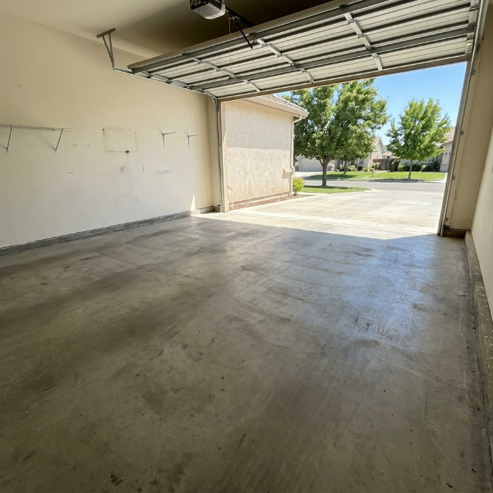 Empty garage with open door, concrete floor, and view of driveway and trees outside.