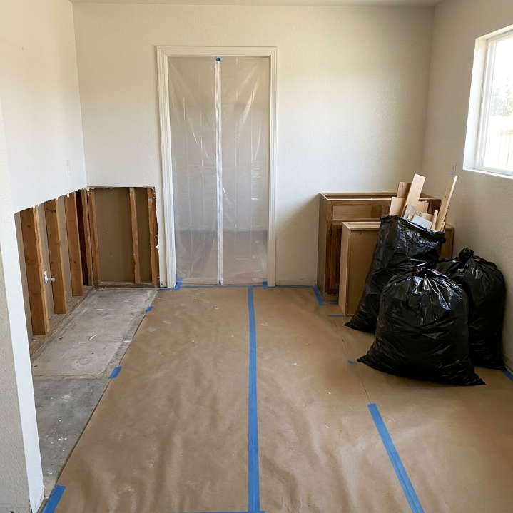 Partially renovated room with plastic-covered doorway, cardboard floor protection, and trash bags near the wall