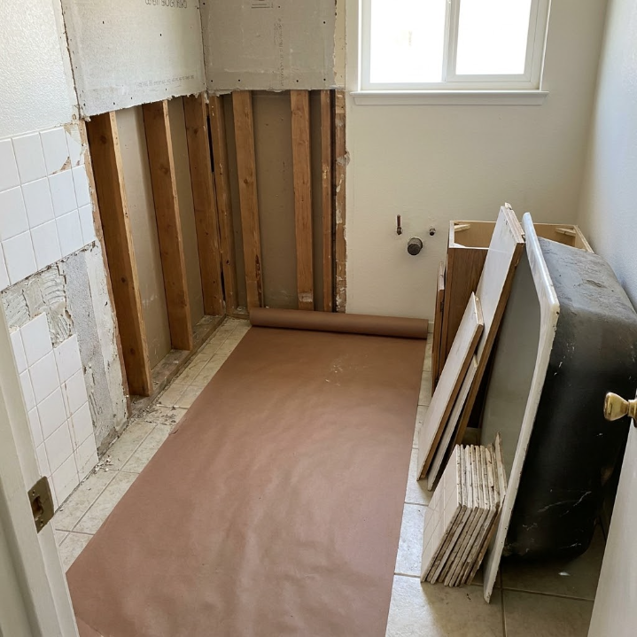 Bathroom under renovation with exposed wall studs, tiled wall, and stacked panels by a window