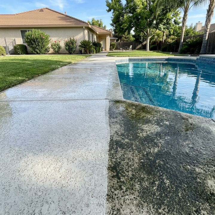 Wet concrete pool deck beside a backyard swimming pool and house on a sunny day