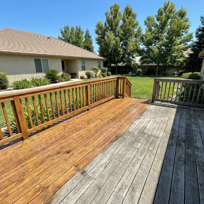 Weathered wooden deck with railing beside a house, overlooking a green backyard and trees.